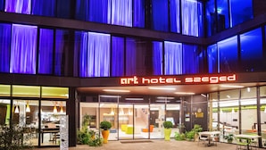 A hotel entrance with a modern design, featuring large windows and a visible reception area. - Art Hotel Szeged (Szeged)