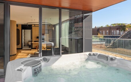 A modern indoor hot tub with a glass enclosure, a wooden ceiling, and a view of a building with a sloped roof.