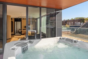 A modern indoor hot tub with a glass enclosure, a wooden ceiling, and a view of a building with a sloped roof.