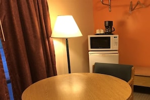 A room with a round wooden table, a lamp, a microwave, and a chair.