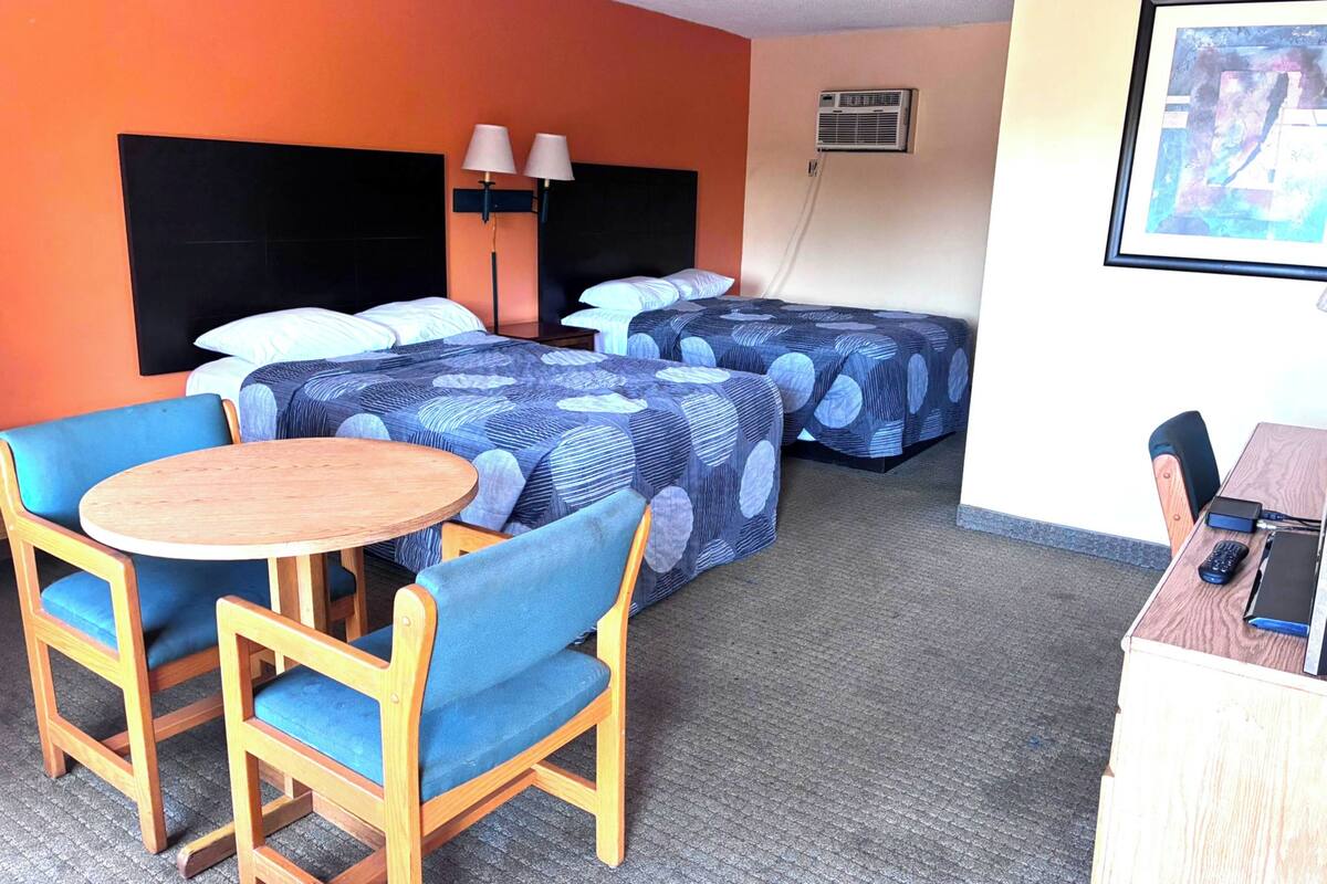 Habitación de hotel con dos camas, un escritorio con una silla, una mesa redonda y un cuadro en la pared.