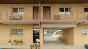 Un edificio de dos pisos con entrada abierta, un letrero que indica una oficina y un área de estacionamiento con líneas azules.