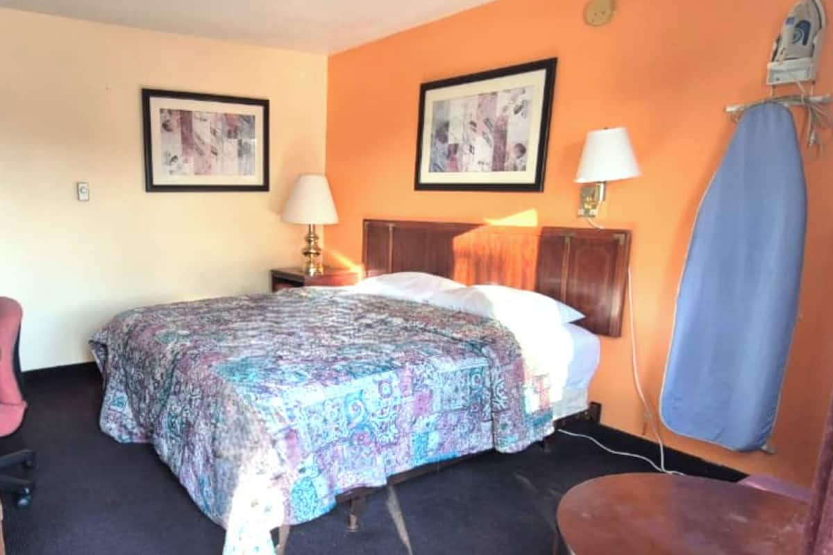 Habitación de hotel con una cama, dos lámparas de pared, una silla y un tablero de planchar azul.