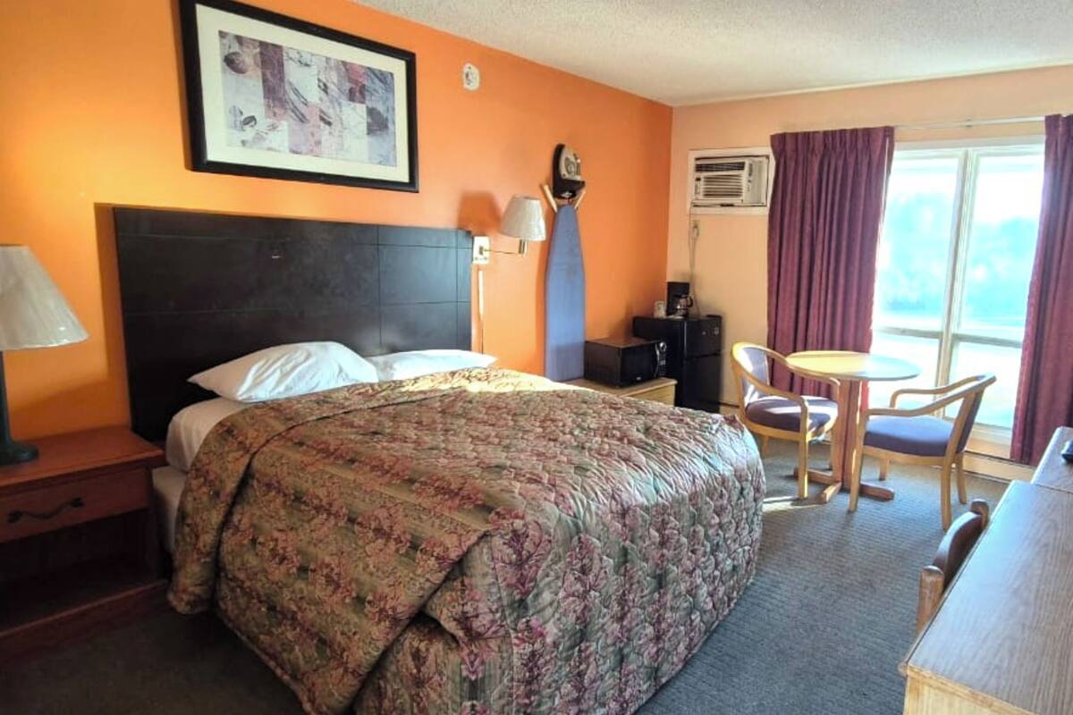 Habitación de hotel con cama, escritorio, silla, lámpara y ventana con cortinas.