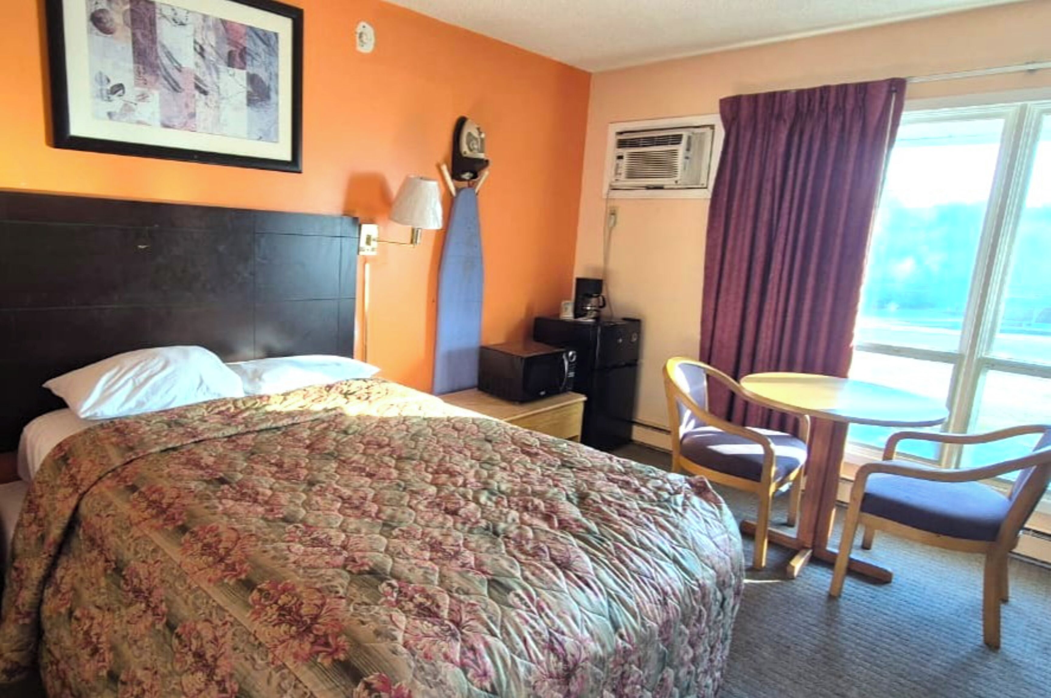 A hotel room with a bed, a desk with a chair, a small table, and a window with curtains.