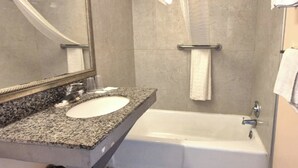 Un baño con lavamanos de encimera de granito, un espejo, una bañera y un perchero para toallas.