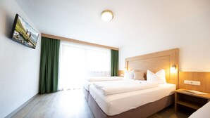 A hotel room with a large bed, a wooden headboard, a bedside table, and a view of the outdoors through a window with green curtains. - Gästehaus Waldesrand (Soelden)