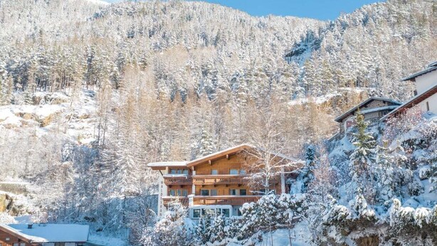 A wooden chalet with a balcony, surrounded by snow-covered trees and mountains. - Gästehaus Waldesrand (Soelden)