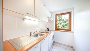 A kitchen with white cabinets, a wooden countertop, a window, and a view of trees outside. - Gästehaus Waldesrand (Soelden)