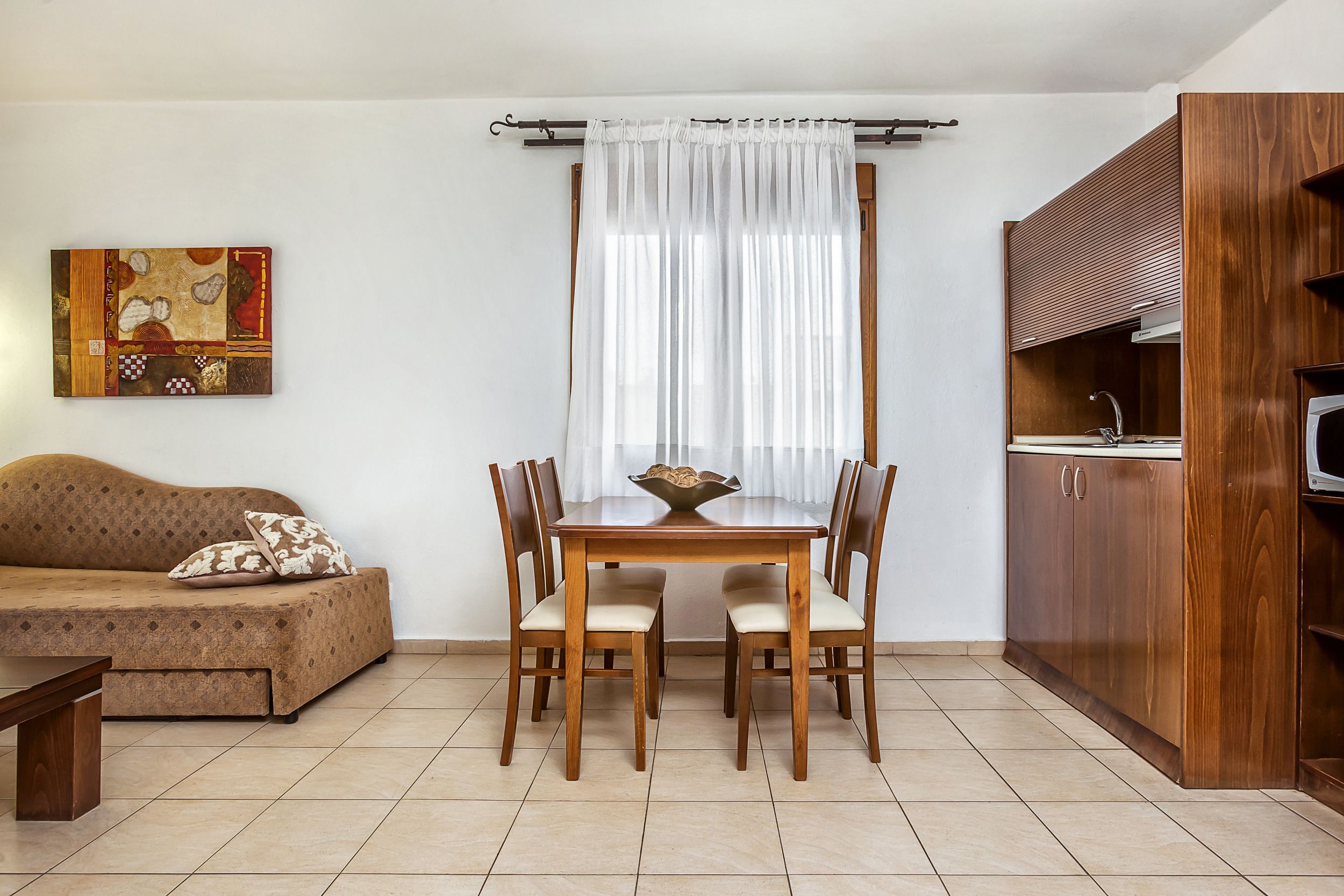 A dining area with a wooden table and chairs, a sofa, and a kitchen area with wooden cabinets.