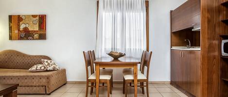 A dining area with a wooden table and chairs, a sofa, and a kitchen area with wooden cabinets.