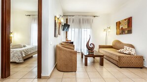 Un salon comprenant un canapé, des fauteuils, une table basse et un téléviseur fixé au mur.