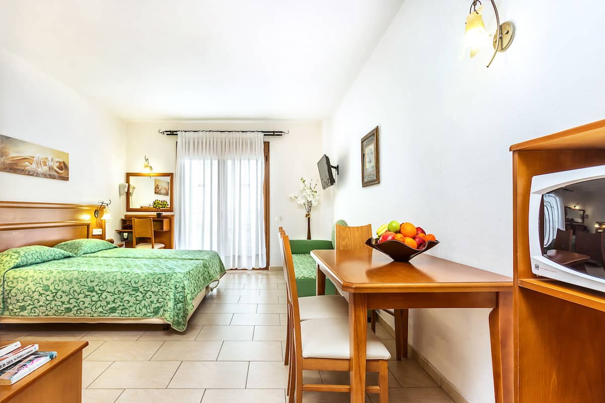Une chambre d’hôtel comprenant un lit, un bureau avec une chaise, une télévision et un panier de fruits.