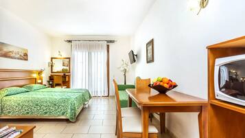 A hotel room with a bed, a desk with a chair, a television, and a fruit bowl.