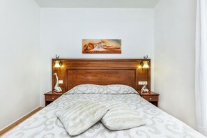 Un lit bien fait, avec une couvre-lit à motifs et des oreillers, une tête de lit en bois agrémentée de lampes murales, et un tableau au-dessus du lit.