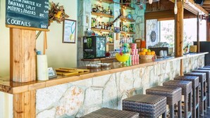 Un espace bar avec un mur en pierre, un comptoir en bois et des tabourets en osier.