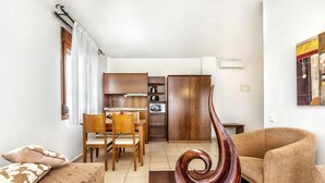 Un salon comprenant un canapé, une table basse et une sculpture moderne. On y trouve également un coin repas avec une table et des chaises, ainsi qu’une cuisine équipée avec des placards et des appareils électroménagers.