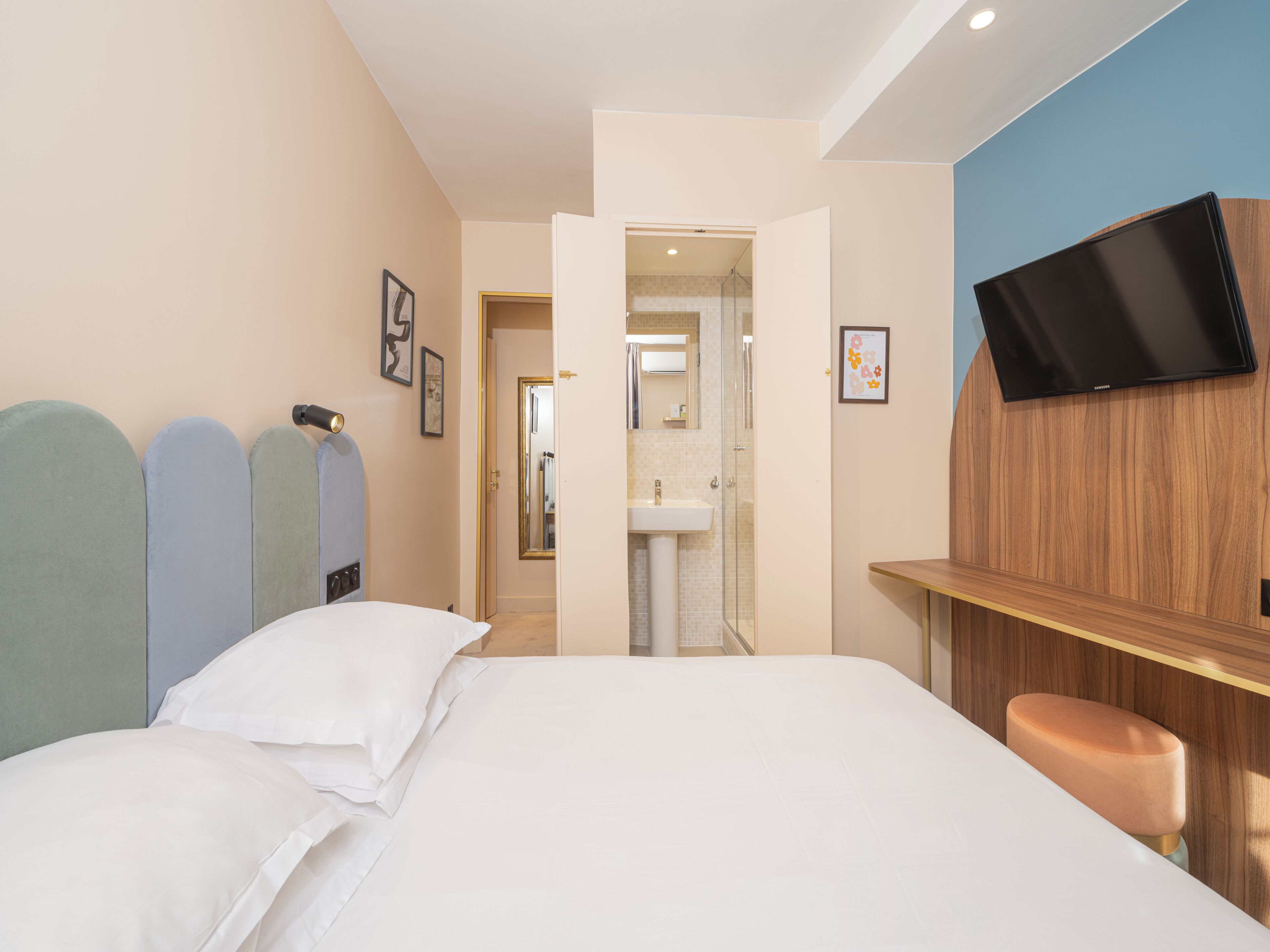 Una camera d'albergo con un letto, una TV a parete, un bagno con lavandino e doccia.