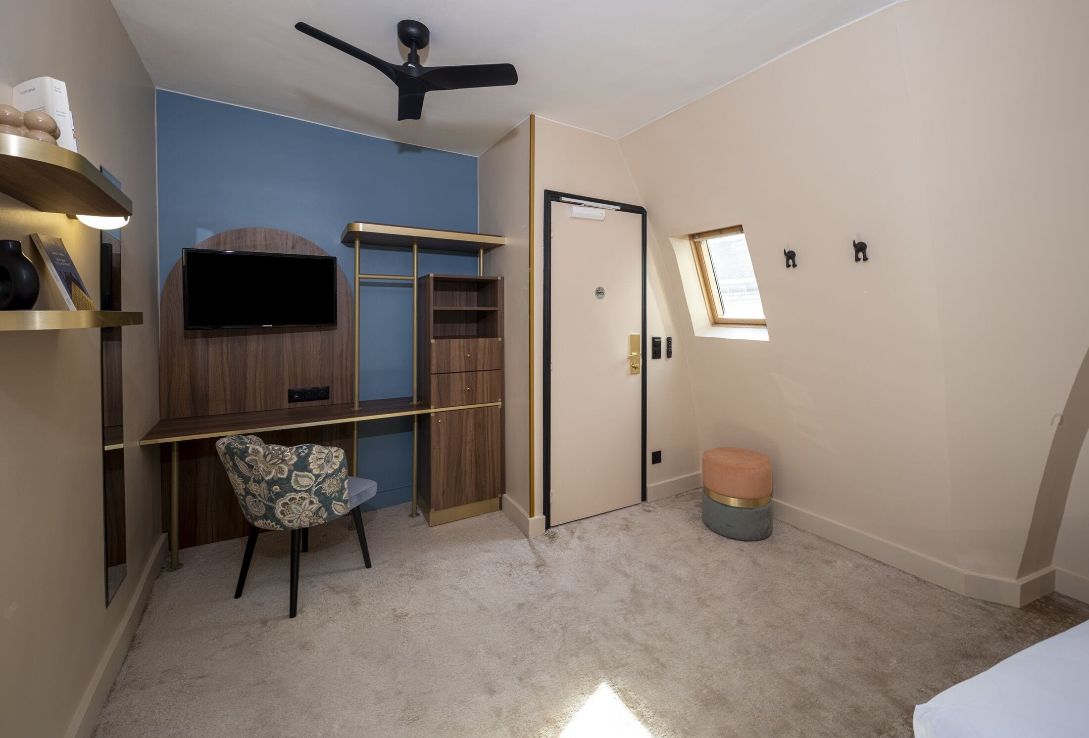 A bedroom with a bed, a desk, a chair, a TV, a wardrobe, a ceiling fan, a window, and a small stool.