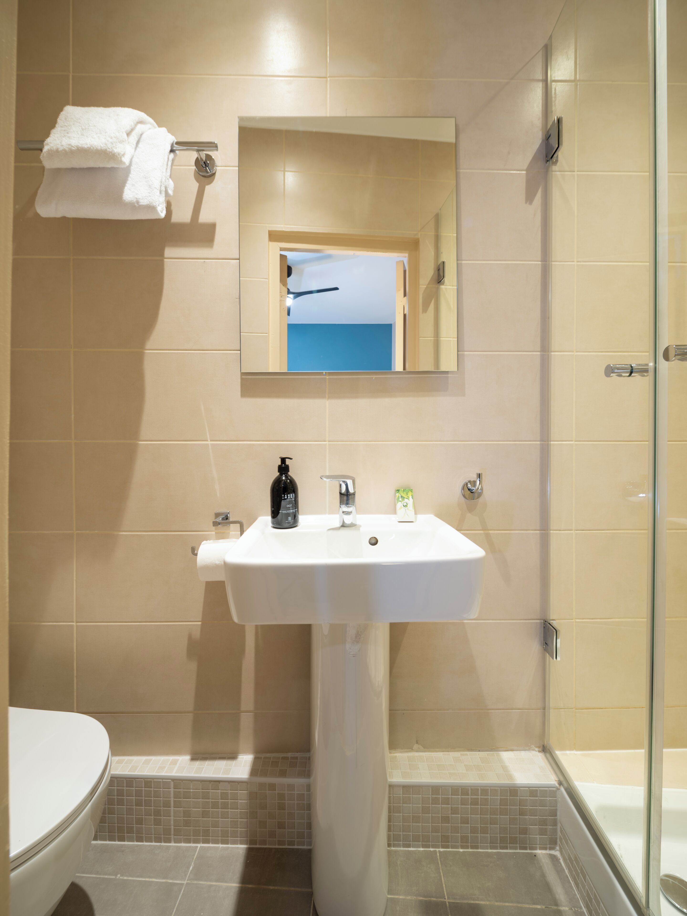 A bathroom with a white sink, a mirror, a towel rack, a toilet, and a shower area.