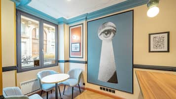 Una habitación con una mesa redonda, dos sillas, una obra de arte grande en la pared y una ventana con vista a la calle.