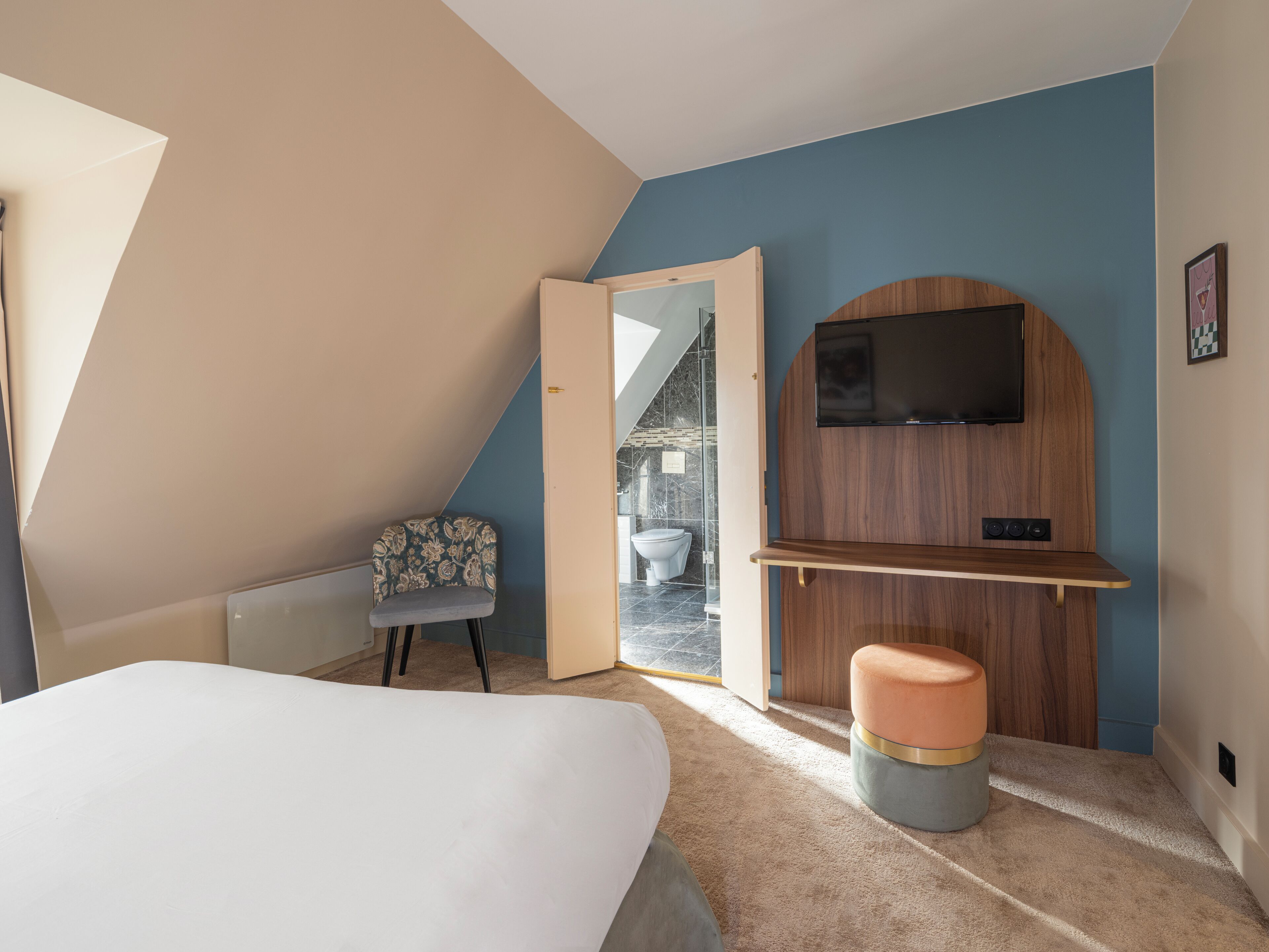 A bedroom with a bed, a chair, a TV mounted on a wooden wall, and a small stool.