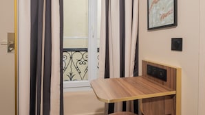 A room with a window, curtains, a small table, and a cushioned stool. - Hotel Boronali Montmartre (Paris)