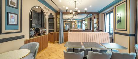 Una cafetería para el desayuno con muebles de madera, mesas con cubierta de mármol y una zona central con sillas acolchadas.