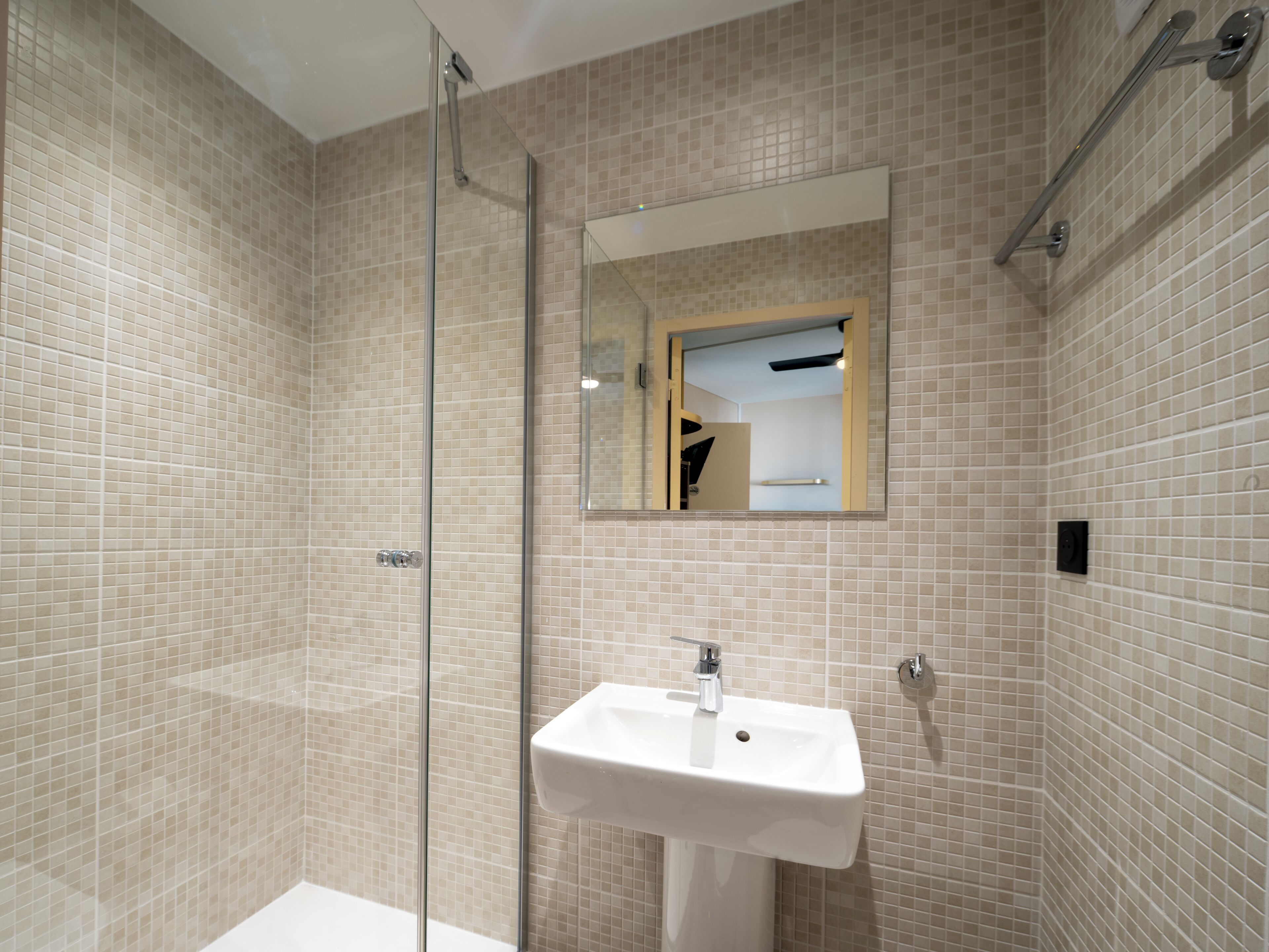 Un baño moderno con cabina de ducha de vidrio, un lavabo blanco y un espejo en la pared.