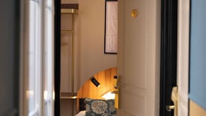 A hotel room with a bed, a bedside table with a lamp, a framed picture on the wall, and a door leading to another room. - Hotel Boronali Montmartre (Paris)