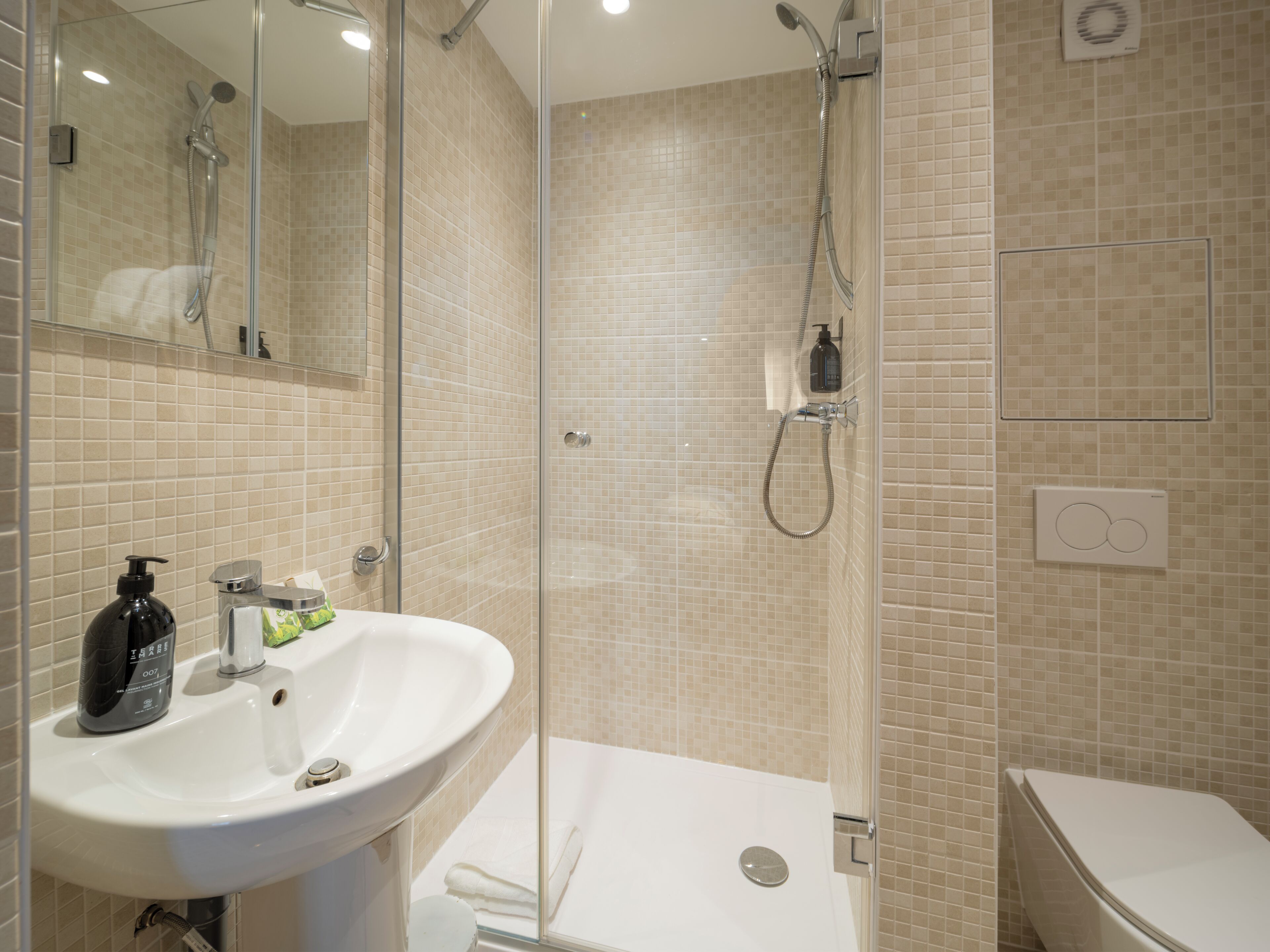 A modern bathroom with a glass-enclosed shower, a white sink with a soap dispenser, and a toilet.