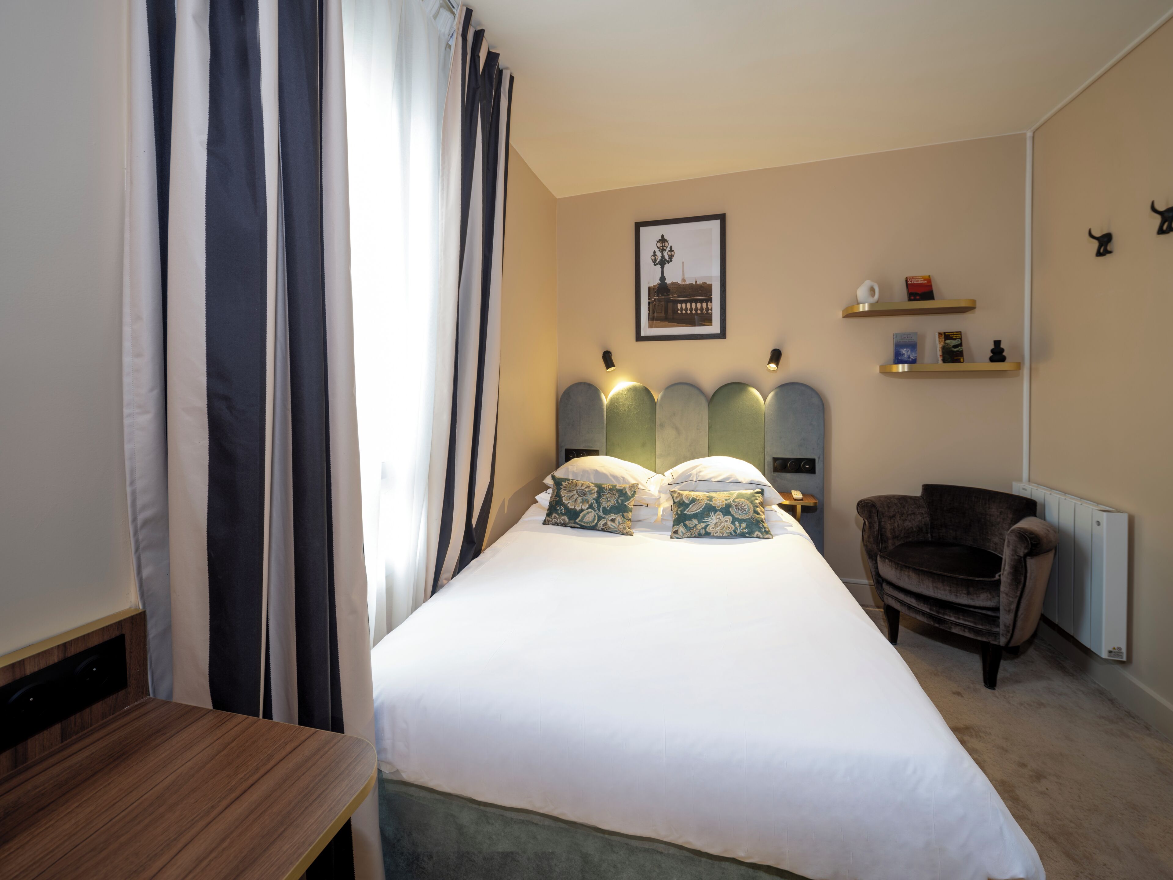 A hotel room with a bed, a chair, a desk, and a radiator.