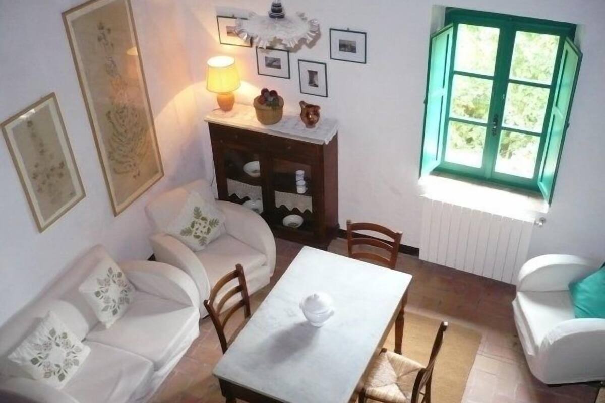 A cozy room with a white sofa, a dining table, and a window with green shutters.
