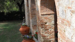 A brick building with arched openings and terracotta planters with flowers. - Caio Alto (Cetona)