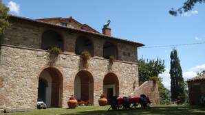 A stone building with arched windows and a tiled roof. There are potted plants and outdoor seating. - Caio Alto (Cetona)