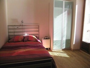 A bedroom with a bed, bedside table, and a sliding glass door leading to a balcony. - Les Z'hirondelles (Annecy)