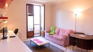 Un salón moderno con un escritorio blanco, un sofá a rayas, una pequeña mesa con esterillas rosas, un plaid verde y una lámpara de pie alta.