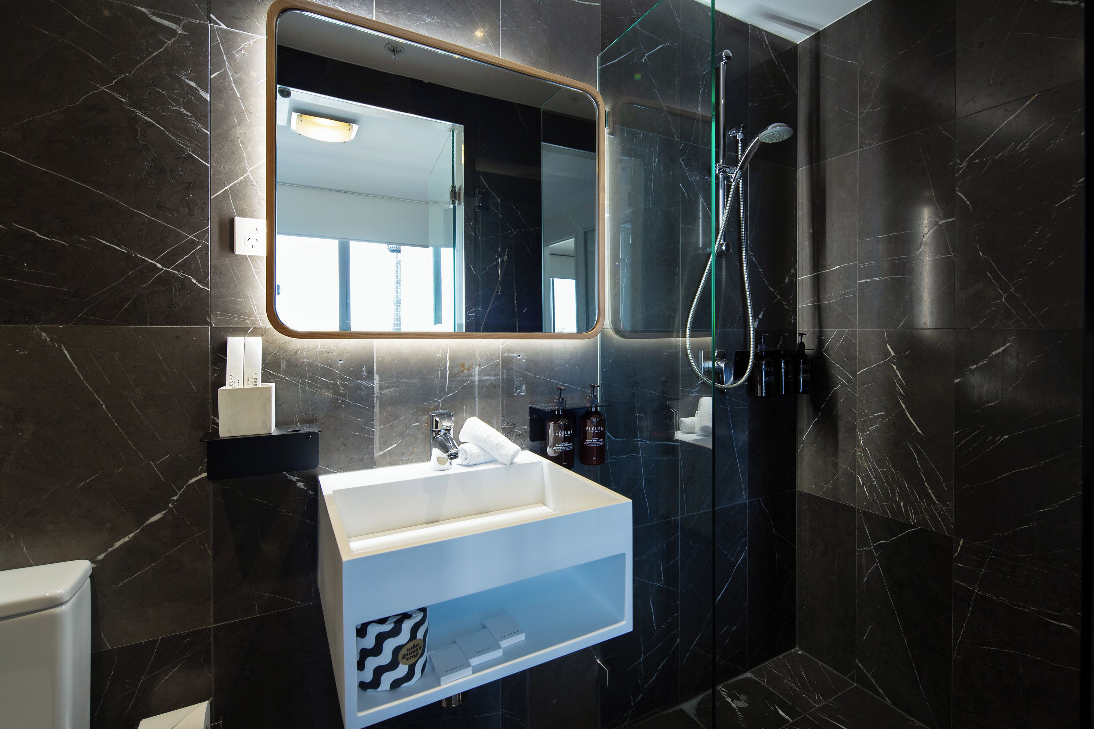 Un baño moderno con un lavamanos de mármol, un espejo grande y una ducha con mampara de vidrio.