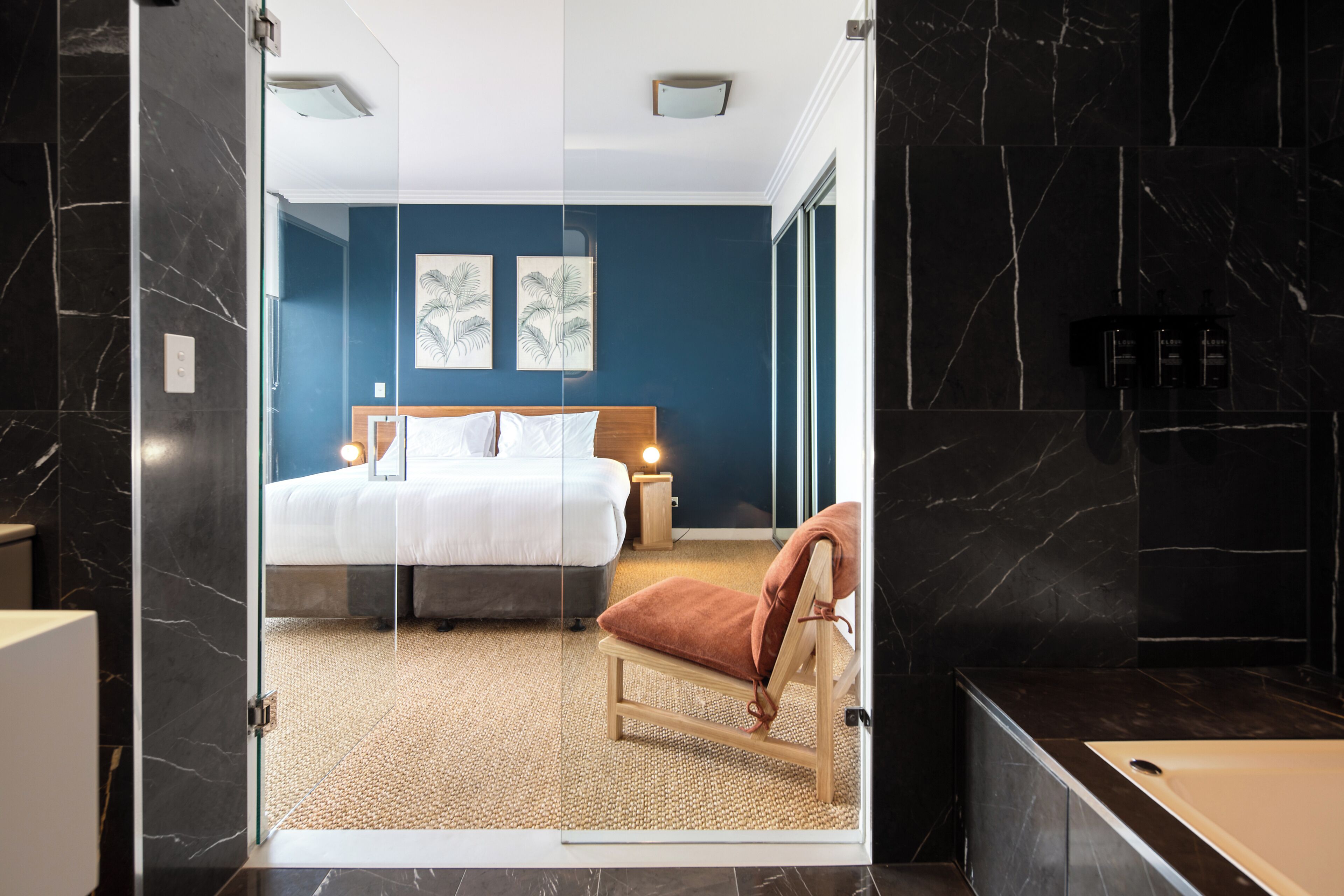 A modern hotel room with a bed, a chair, and a bathroom with a bathtub.