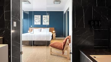 A modern hotel room with a bed, a chair, and a bathroom with a bathtub.