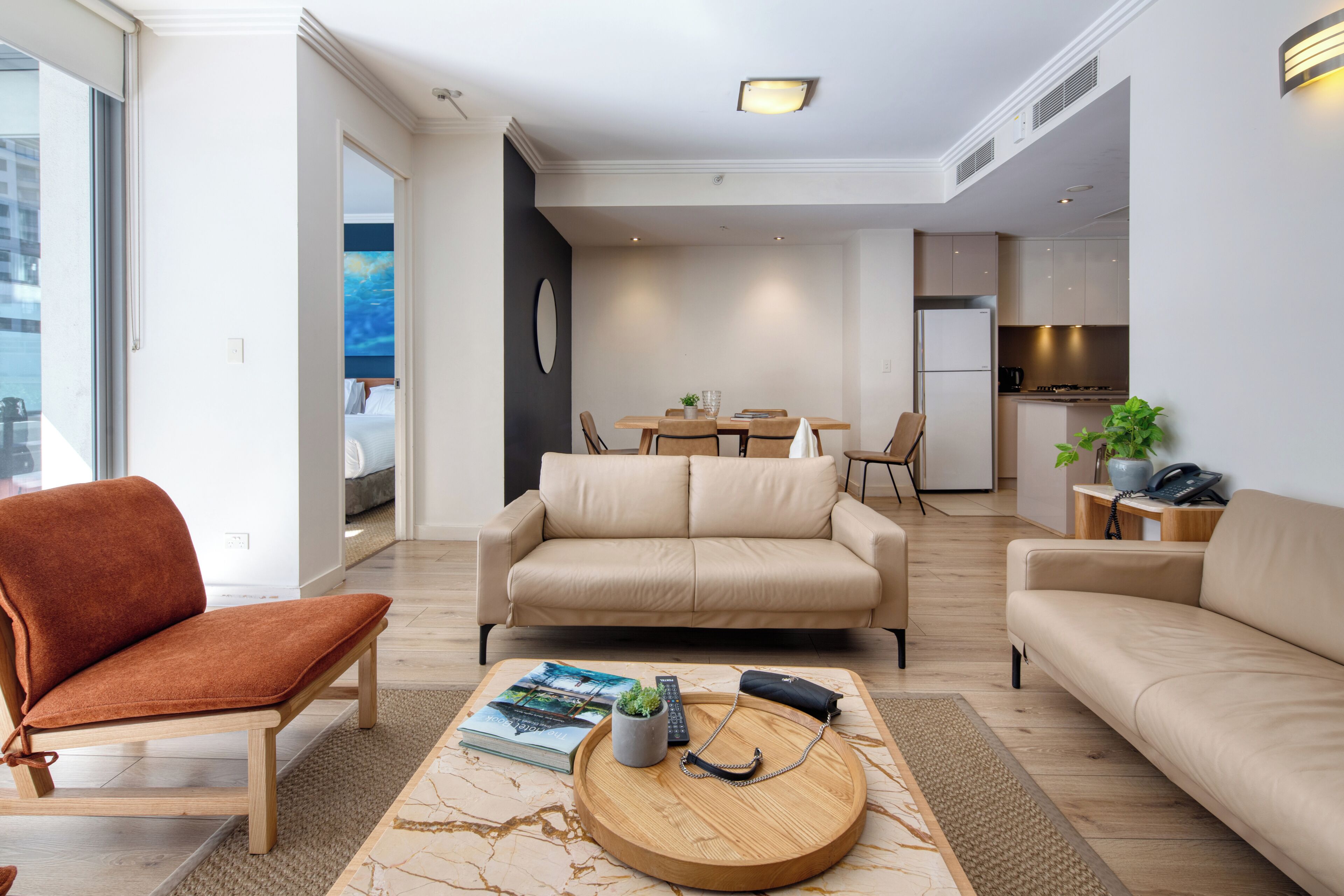 Una sala moderna con sofá, sillón y mesa de centro, un comedor con sillas, y una cocina con refrigerador y estufa.