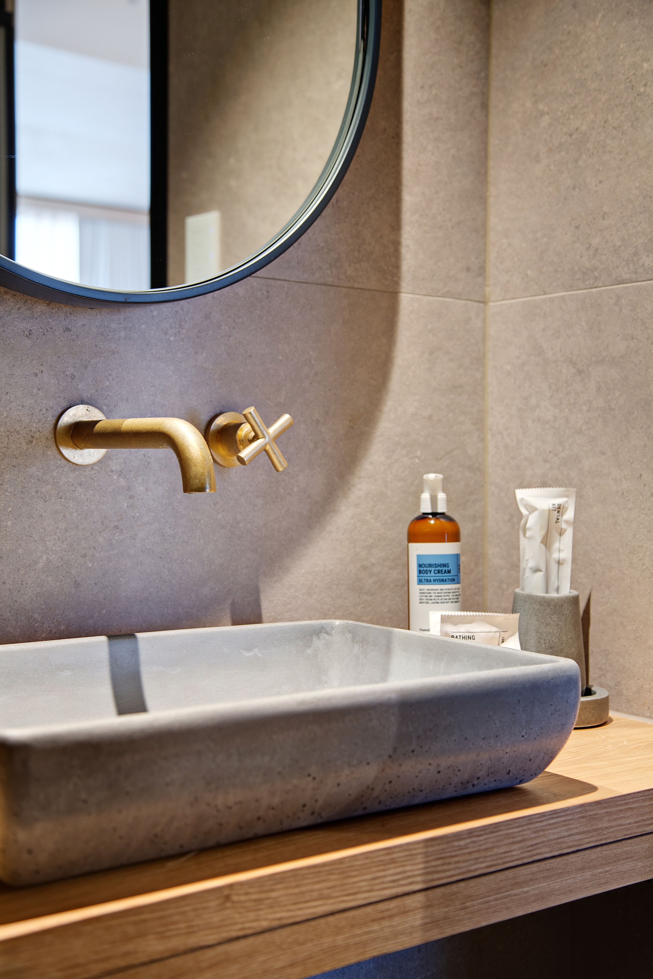 Ein Badezimmer mit einem modernen Waschbecken, einem goldenen Wasserhahn und einem runden Spiegel.