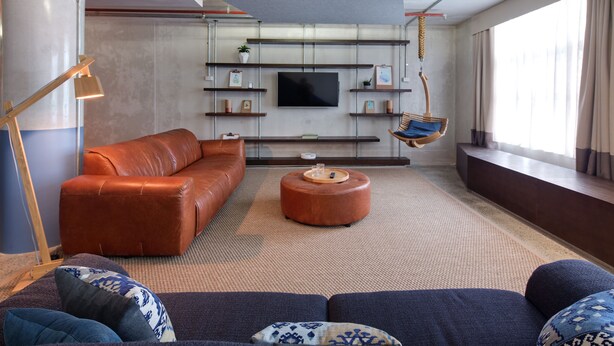A modern living room with a leather sofa, a round ottoman, and a hanging chair. - Zara Tower Hotel (Sydney)