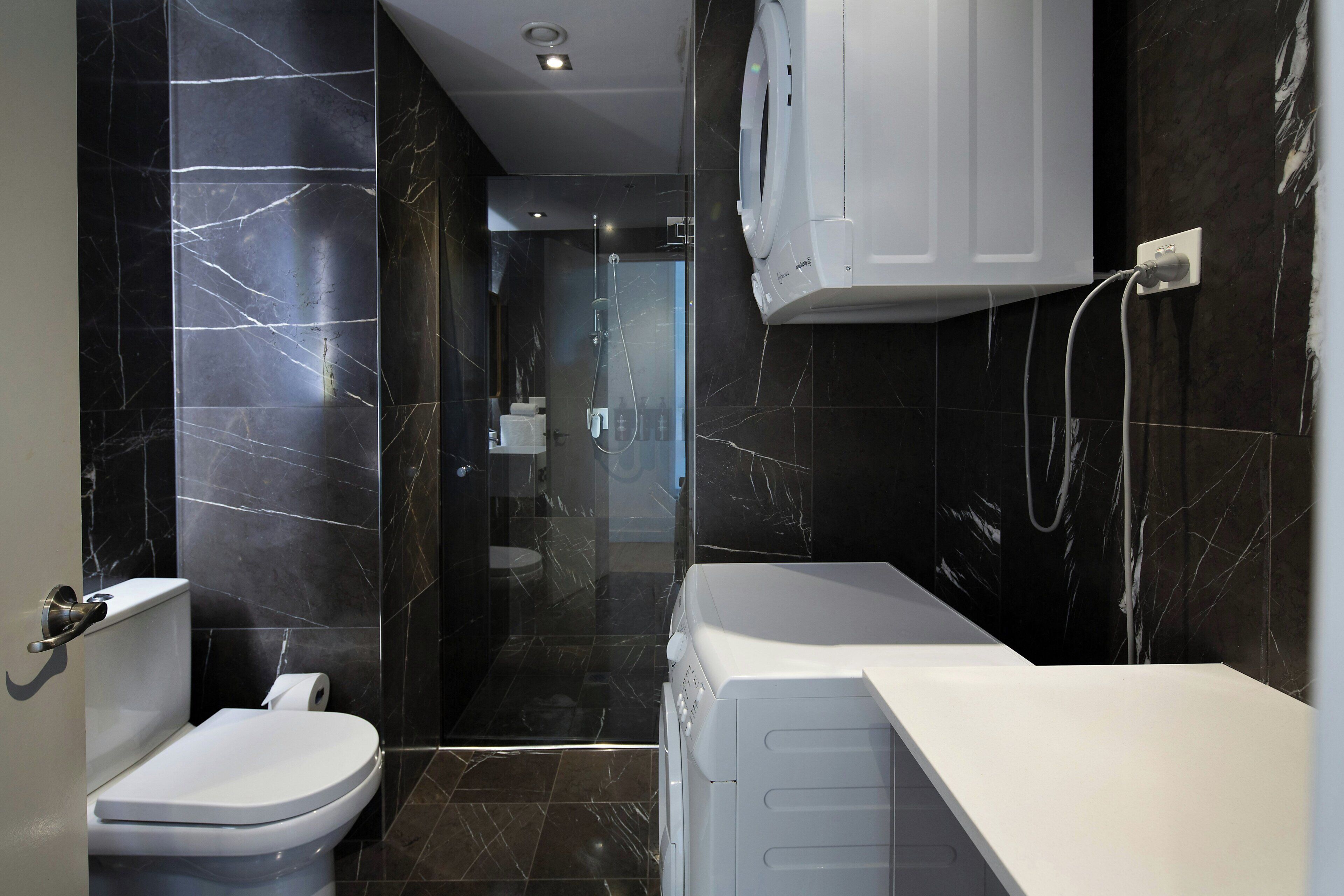 A modern bathroom with a toilet, a shower, and a built-in washing machine.