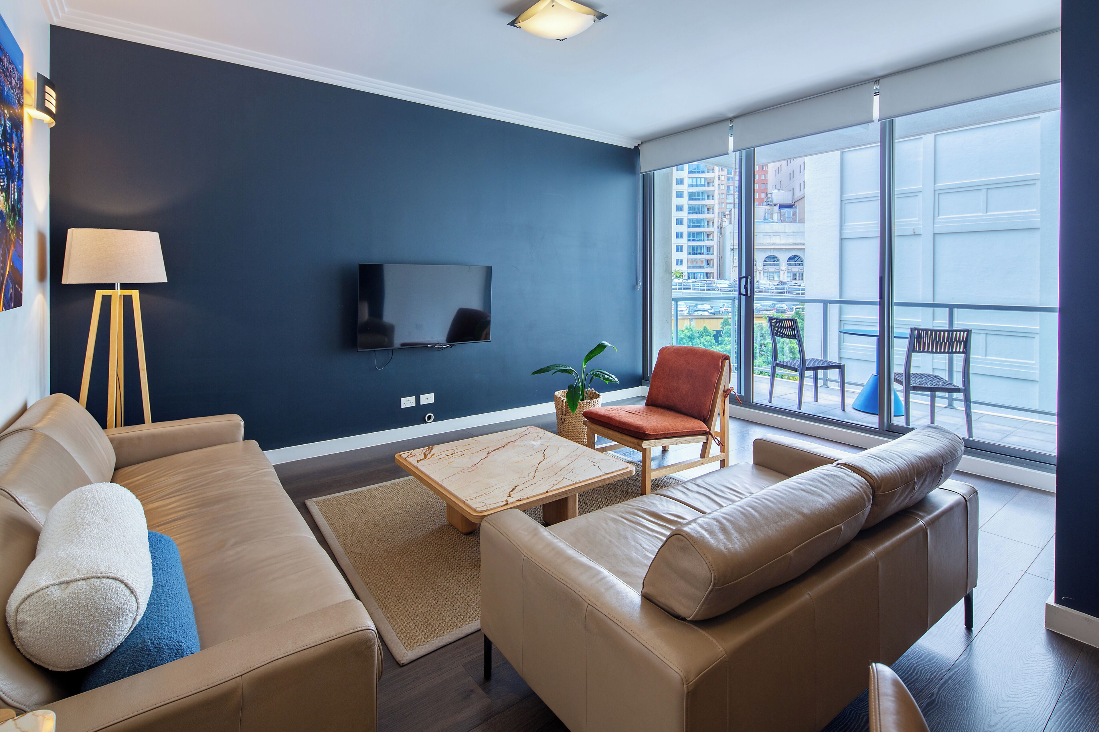 Una sala moderna con sofá, sillón y mesa de centro, televisor de pantalla plana y balcón con mobiliario exterior.