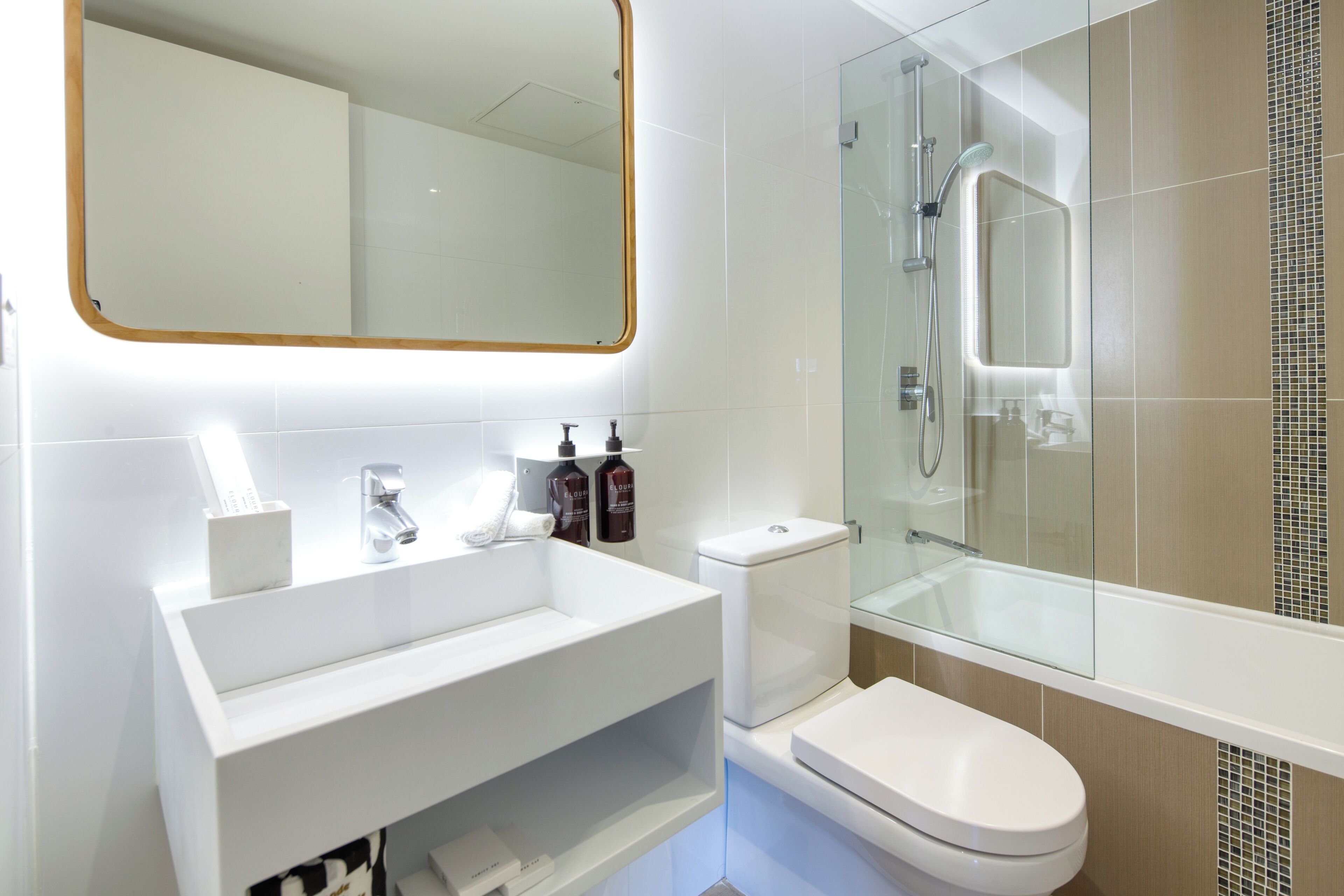 Un baño moderno con lavamanos blanco, inodoro y ducha con mampara de vidrio.