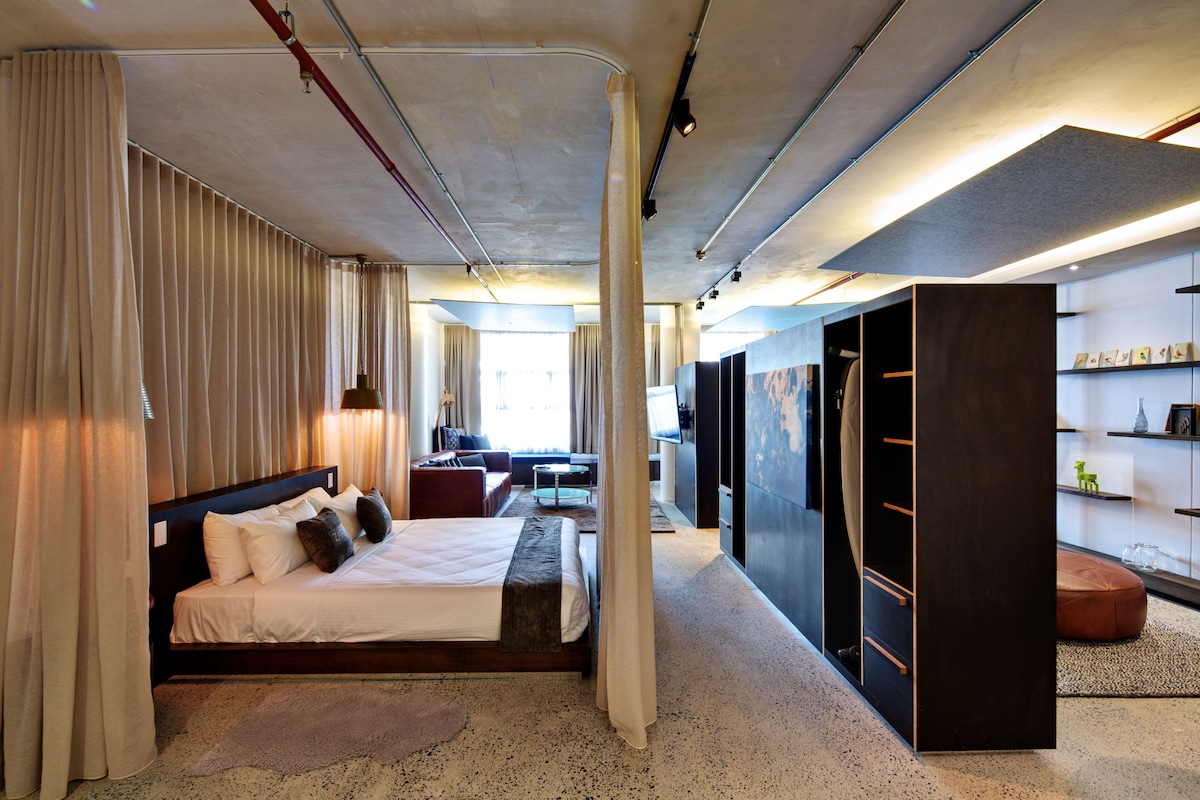 A modern hotel room with a large bed, a seating area, and a walk-in closet.