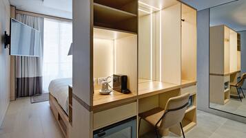 Una habitación de hotel moderna con una cama, un escritorio con una silla, una cafetera y un espejo grande.