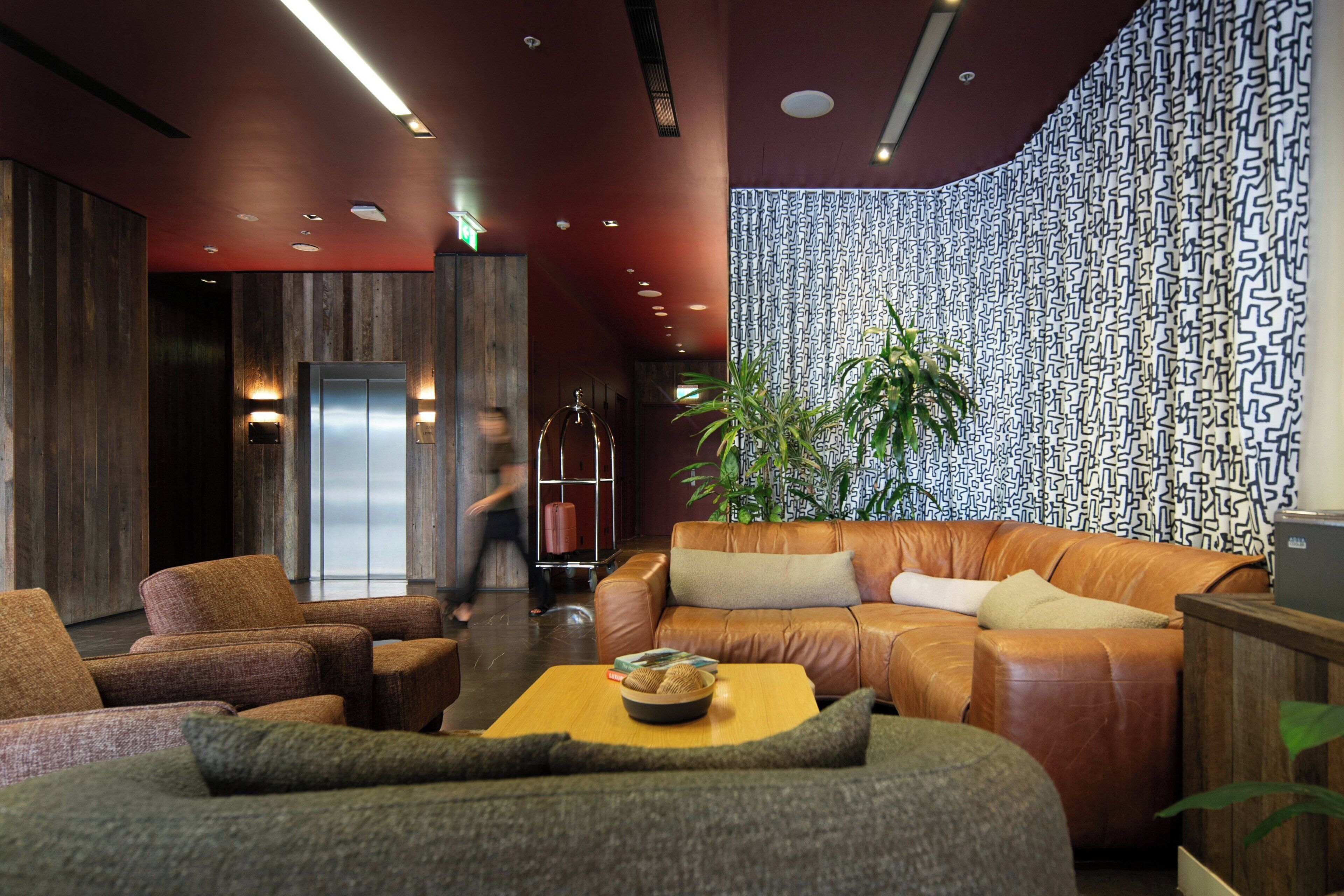 A lobby with a leather sofa, armchairs, a coffee table, a patterned wall, and a plant.