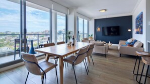 A spacious living area with a dining table, chairs, a sofa, and a TV. - Zara Tower Hotel (Sydney)